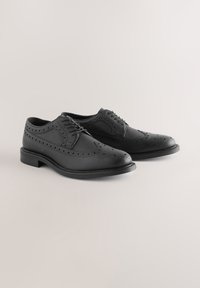 Chaussures noires à lacets en cuir texturé, avec des perforations détaillées, un bout arrondi et un talon bas solide noir.