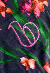 Lilleline kangas tumeda taustaga, kus on roosad ja oranžid lilled. Esiplaanil on tikitud roosa number "10", mis on hästi nähtav.