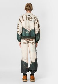 Conjunto de sudadera y pantalones de chándal en beige con diseño de montañas. Presenta un diseño oversize, puños elásticos y acentos en verde contraste.