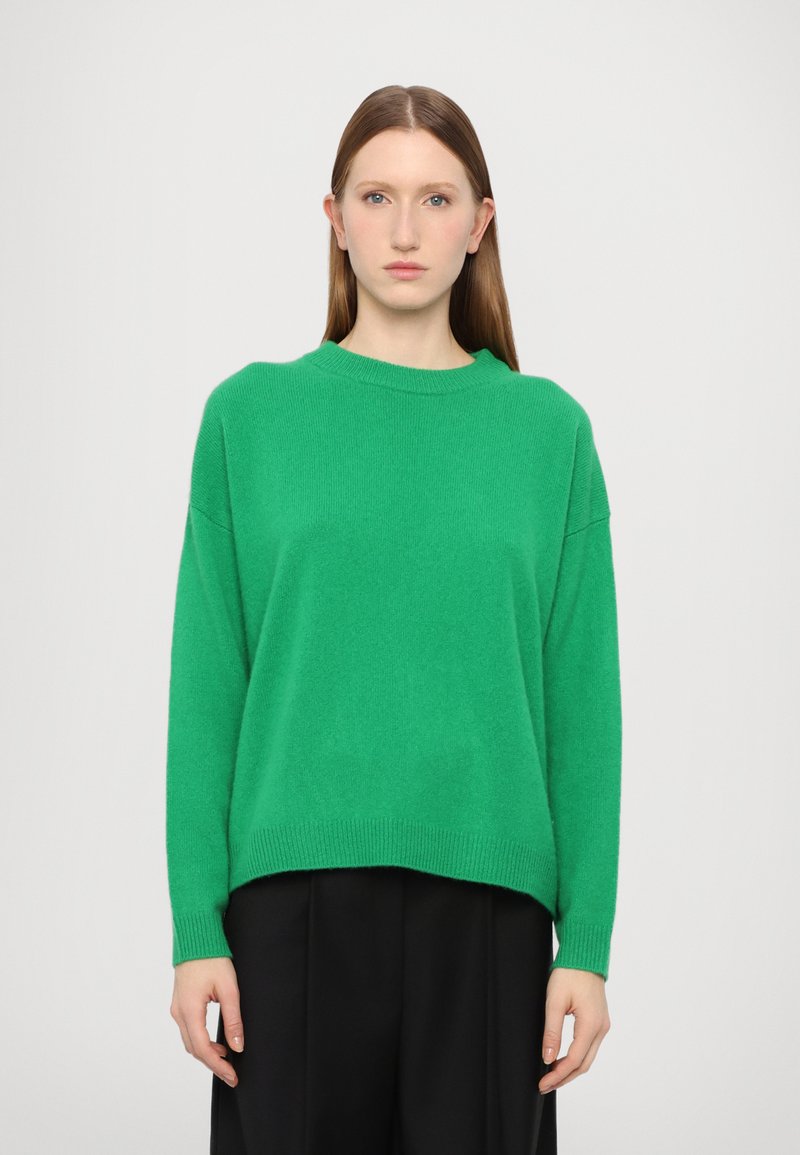 Green sweater made of soft knit material, featuring a round neckline, dropped shoulders, and ribbed hem. Worn with black pants.