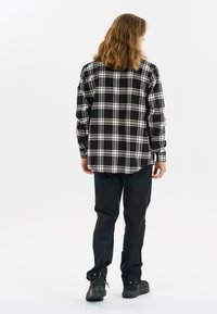 Zwart-wit geruite flanellen overhemd met lange mouwen, knoopsluiting aan de voorkant en een relaxte pasvorm, gecombineerd met donkere broek en robuuste zwarte schoenen.