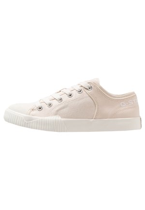 Lavtop beige lærredsneaker med hvid gummisål, metaløjer og snørebånd, med diskret branding på hælsiden.