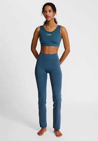 Sport-bh i teal och matchande högmidjade leggings, båda gjorda av elastiskt material. Har en logotyp på bh:n, åtsittande design och slät textur.