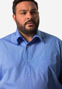 Světlomodrá košile na knoflíky s kapsou, vyrobená z hladkého materiálu. Má klasický límec a jemnou texturu.