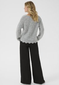 Pulover tricotat gri deschis, cu mâneci lungi, guler ribbed și tiv ondulat, asortat cu pantaloni negri largi, cu picioare largi.