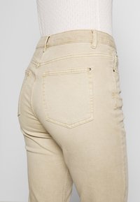 Jeans de mezclilla beige con una textura suave, corte ajustado y dos bolsillos traseros con sutiles detalles de costura.