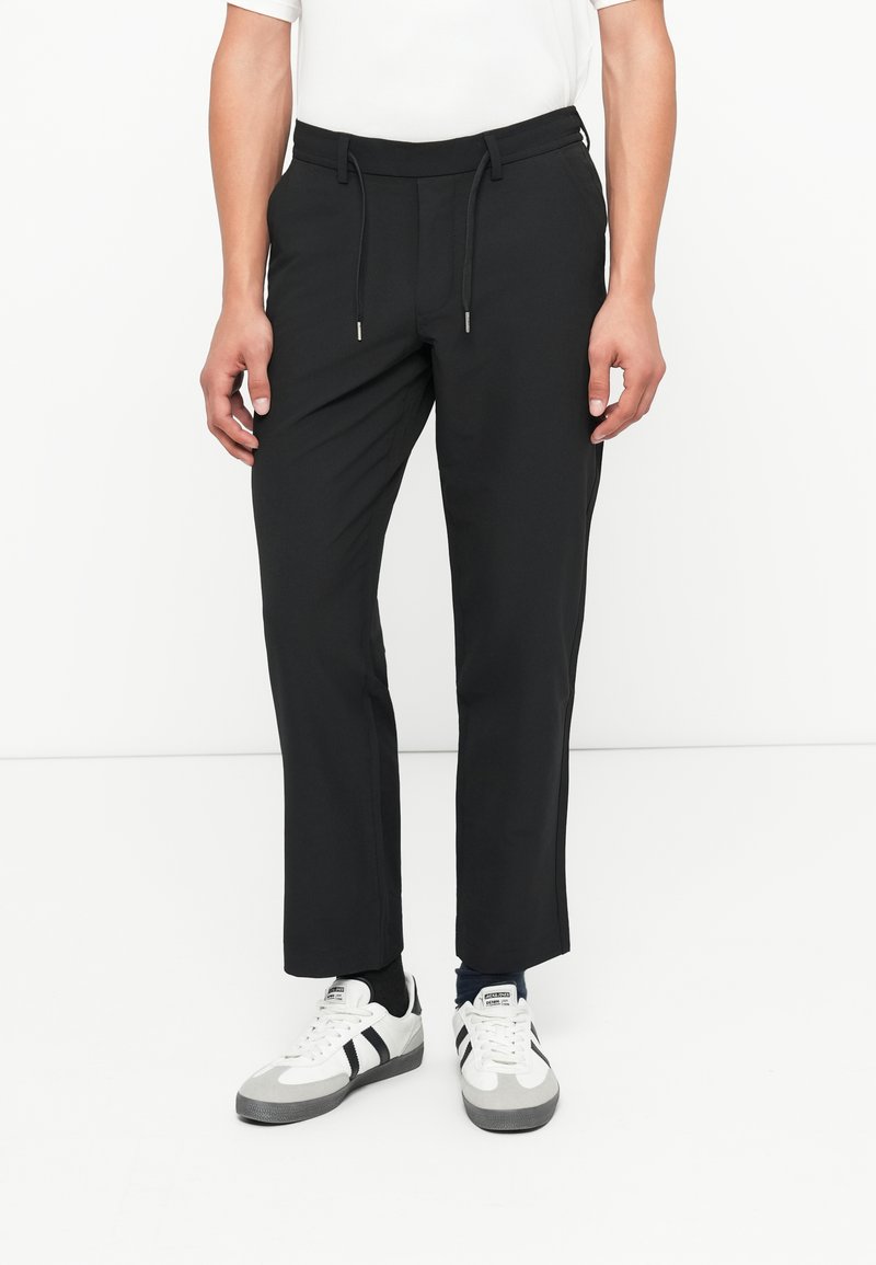 Pantaloni sport negri, cu talie elastică, șnururi ajustabile și croi drept. Asortați cu adidași albi și gri.