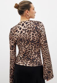 Leopard print long-sleeve top in soft fabric with a fitted silhouette and flared sleeves, featuring shades of brown, beige, and black.