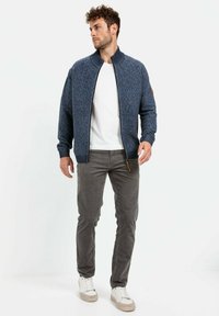 Blauwe gebreide bomberjack met een gestructureerd oppervlak, ribgebreide kraag en manchetten. Draag over een witte shirt en gecombineerd met grijze broek en sneakers.