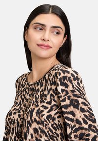 Blouse à imprimé léopard avec un col rond, une texture plissée, des couleurs noire et beige, et des manches longues. Tissu doux et fluide.