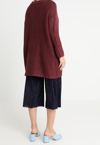 Burgundyröd stickad oversized tröja med ribbade ärmar, i kombination med marinblå plisserade culotter och ljusblå klackskor med blockklack.