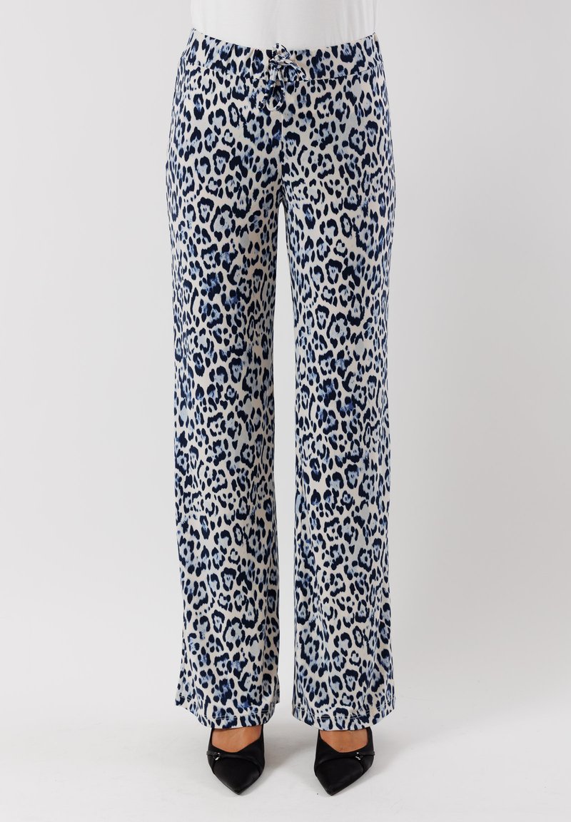 Pantaloni larghi a stampa leopardata in crema con macchie blu, dotati di un elastico in vita e realizzati in un tessuto morbido e liscio. Sono indossate scarpe nere con tacco a punta.