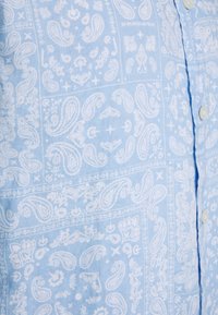 Tessuto azzurro chiaro con motivi paisley e floreali bianchi, con bottoni lungo una cucitura verticale.