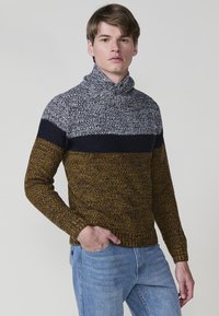 Gebreide coltrui in een ontwerp met kleurblokken in grijs, marineblauw en mosterd, met een gestructureerde afwerking. Draagt met lichtblauwe jeans.