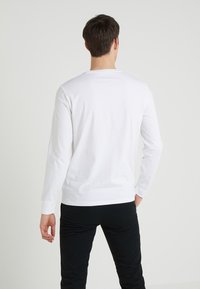 Vit långärmad T-shirt i bomull med rund hals och avslappnad passform, kombinerad med svarta byxor. Enkelt utseende, inga mönster eller dekorationer.