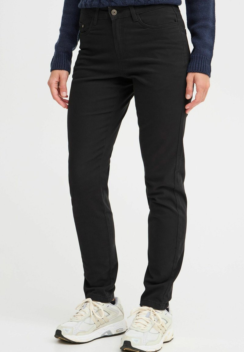 Black skinny jeans with a smooth texture, featuring a front button closure and pockets. Worn with light-colored athletic shoes.