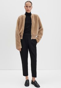 Giacca bomber in fleece colore beige con finitura textured, pantaloni neri affusolati e mocassini neri. Design semplice con polsini e orlo a coste.