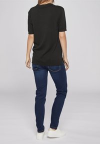 Černý top s krátkým rukávem a volným střihem, spojený s tmavě modrými džíny slim fit a bílými teniskami, viděný zezadu.