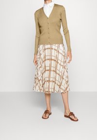 Beige pletený cardigan s výstřihem do V, šesti knoflíky, zkombinovaný s plisovanou midi sukní se vzorem v krémové a hnědé barvě. Nošený s hnědými šlapkami.