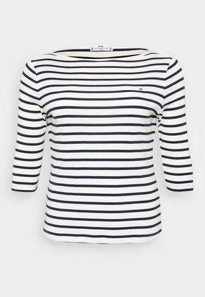 Stripet topp med båtutringning. Laget av myk stoff med horisontale marineblå og hvite striper. Design med tre fjerdedels ermer.