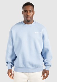 Lichtblauwe sweatshirt gemaakt van zacht materiaal, met een ronde kraag en een geribde onderkant. Witte "SMILODOX Ltd." logo op de voorkant.
