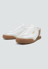 Białe sneakersy z gładką cholewką, zamszowymi akcentami i brązową gumową podeszwą. Oferują złote logo i sznurowaną konstrukcję.