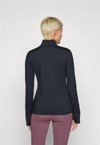 Maglietta nera a maniche lunghe con collo alto e design aderente, realizzata in materiale elasticizzato, abbinata a leggings viola a vita alta.