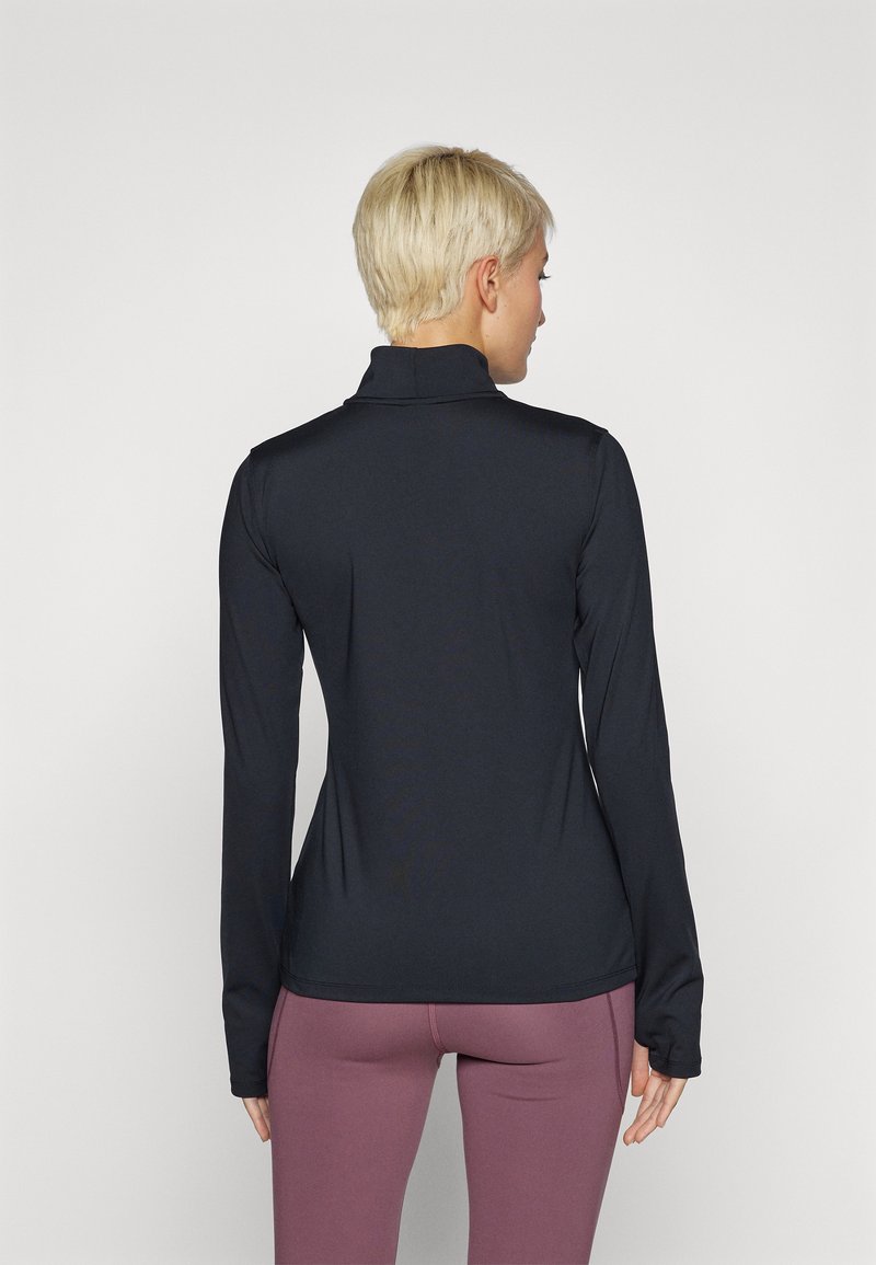 Maglietta nera a maniche lunghe con collo alto e design aderente, realizzata in materiale elasticizzato, abbinata a leggings viola a vita alta.