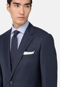 Jūras spēku zila blazer jakas ar teksturētu apdari, ar uzplatu apkaklēm un krūšu kabatu, kurā ir balts kabatlakats. Apvienots ar gaiši zilu svītrainu kreklu un punktiņu kaklasaiti.