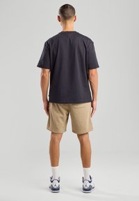 T-shirt grigio scuro a maniche corte, in cotone, vestibilità ampia, abbinato a pantaloni corti color khaki, design semplice. Le scarpe da ginnastica bianche completano il look.