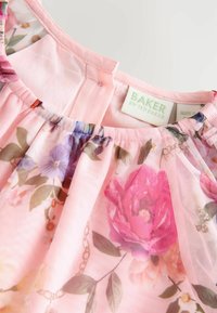 Ziedu kleita ar rozā caurspīdīgu audumu, kurā ir purpursarkanas un rozā ziedu raksti, savilktā apkakle un etiķete ar tekstu "BAKER by Ted Baker."