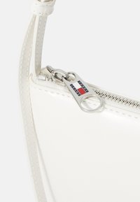 White synthetic handbag with a smooth texture. Features a silver-tone zipper pull with a logo tag and contrasting stitching detail.