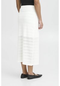 Witte midi rok van textuurgebreide stof met horizontale strepen, gecombineerd met zwarte ballerina's. Het ontwerp is eenvoudig en elegant.