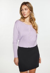 Cardiganul ajustat de culoare lila, realizat dintr-un material moale, cu mâneci lungi și șase nasturi decorativi. Este asociat cu o fustă neagră ajustată.