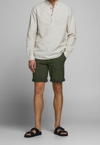 Béžová dlouhá halenka s knoflíkovou légou, v kombinaci s olivově zelenými zkrácenými šortkami a černými sandály. Neformální oblečení s uvolněným střihem.