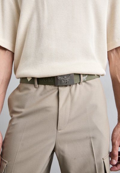 Beige teksturert skjorte, olivenbelte med logoed metallspenne, og lyse khaki bukser med sidelommer og rene søm detaljer.