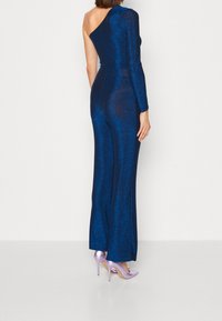 En axel, glittrig blå jumpsuit med en åtsittande silhuett och utsvängda ben, kombinerad med lavendelfärgade stilettklackar.