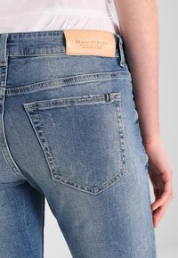 Jeans de mezclilla azul claro con un parche de cuero etiquetado "Marc O'Polo" en la cintura. Presentan un diseño tradicional de bolsillo trasero y costuras.
