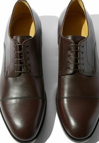 Scarpe da uomo in pelle marrone con finitura liscia, punte arrotondate, design con lacci e cuciture decorative lungo la punta e i lati.