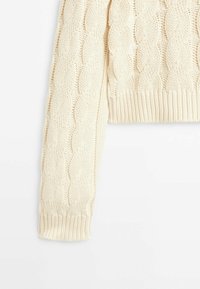 Pull court de couleur crème avec une texture en maille torsadée. Présente des poignets et un ourlet côtelés, montrant un design en maille détaillé sur l'ensemble.
