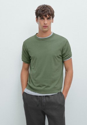 Maglietta a maniche corte verde oliva con scollo rotondo e uno strato sottostante grigio chiaro. Tessuto liscio, design aderente, abbinata a pantaloni grigio scuro.