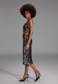 Musta paljetein varustettu kahdesta osasta koostuva asu, jossa on olkaimeton lyhyt toppi ja polvimittainen hame. Yhdistetty teräväkärkisiin mustiin korkokenkiin.