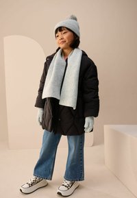 Melna pufota jaka, gaiši zila adīta šalle un cepure ar pom-pomu, pelēki cimdi, platākā kājā džinsu bikses un rakstainas kurpes ar platformu.