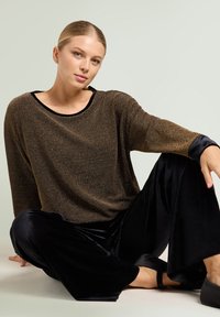 Pantalon ample en velours noir associé à un haut fluide orné de fils dorés avec un col et des poignets noirs. Texture lisse avec une coupe décontractée.