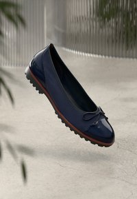Marineblaue Ballerinas mit glänzender Lackspitze, strukturiertem Obermaterial, kleinem Schleifenakzent und einer flexiblen Gummisohle mit Profil.