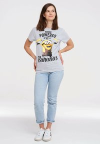 Gray cotton t-shirt featuring a colorful Minion graphic and the text "Powered by Bananas." Slim fit, round neckline. Paired with light blue jeans.