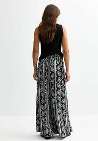Top noir sans manches associé à un pantalon large à rayures noir et blanc, présentant des motifs floraux et une taille élastique.