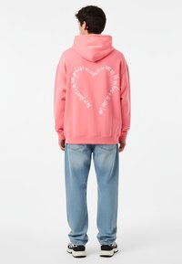 Felpa rosa con una grande scritta bianca sul retro, abbinata a jeans azzurri chiari e sneakers nere. Tessuto morbido e vestibilità comoda.