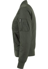 Oliwkowa bombka z dopasowaną kołnierzykiem, ściągaczami przy mankietach, bocznymi kieszeniami oraz kieszenią zapinaną na zamek na lewym rękawie. Gładka faktura materiału.