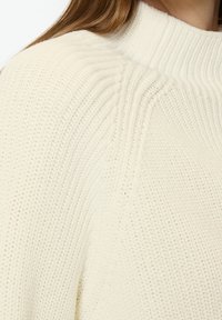 Pull tricoté couleur crème avec un col montant côtelé, une coupe décontractée et un motif texturé sur tout le tissu.